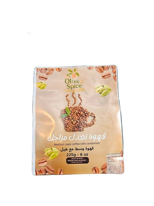 A stand-up pouch of Olive Spice cinnamon coffee, medium roast, 225g, placed on a black textured leather surface. The packaging features a beige label with coffee beans, green cinnamon pods, and a coffee cup graphic.

