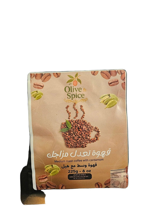 A black stand-up pouch of Olive Spice medium roast coffee with cardamom, featuring a beige front label with coffee beans, a coffee cup graphic, and Arabic text, photographed on a dark textured surface.